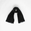 A black fluffy scarf with fringed ends is laid out against a plain white background.