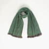 A green alpaca wool scarf with fringed ends is laid out against a plain white background.